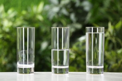 Photo of Empty, half and full glasses of water on white table against blurred background