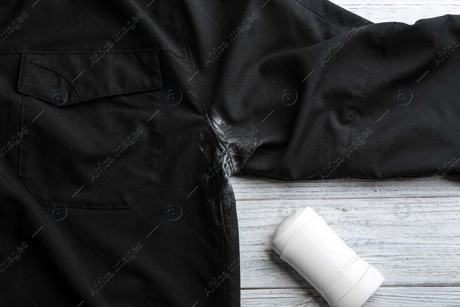 Photo of Black shirt with stain and deodorant on white wooden background, top view