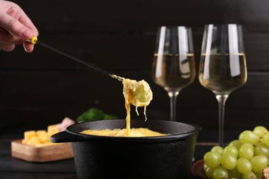 Photo of Dipping grape into fondue pot with melted cheese on table, closeup