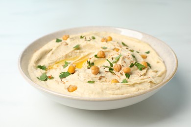 Photo of Tasty hummus with garnish in bowl on white table, closeup