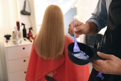 Photo of Professional hairdresser holding bowl with hair dye in beauty salon, closeup