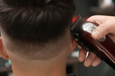 Photo of Professional barber making stylish haircut in salon, closeup