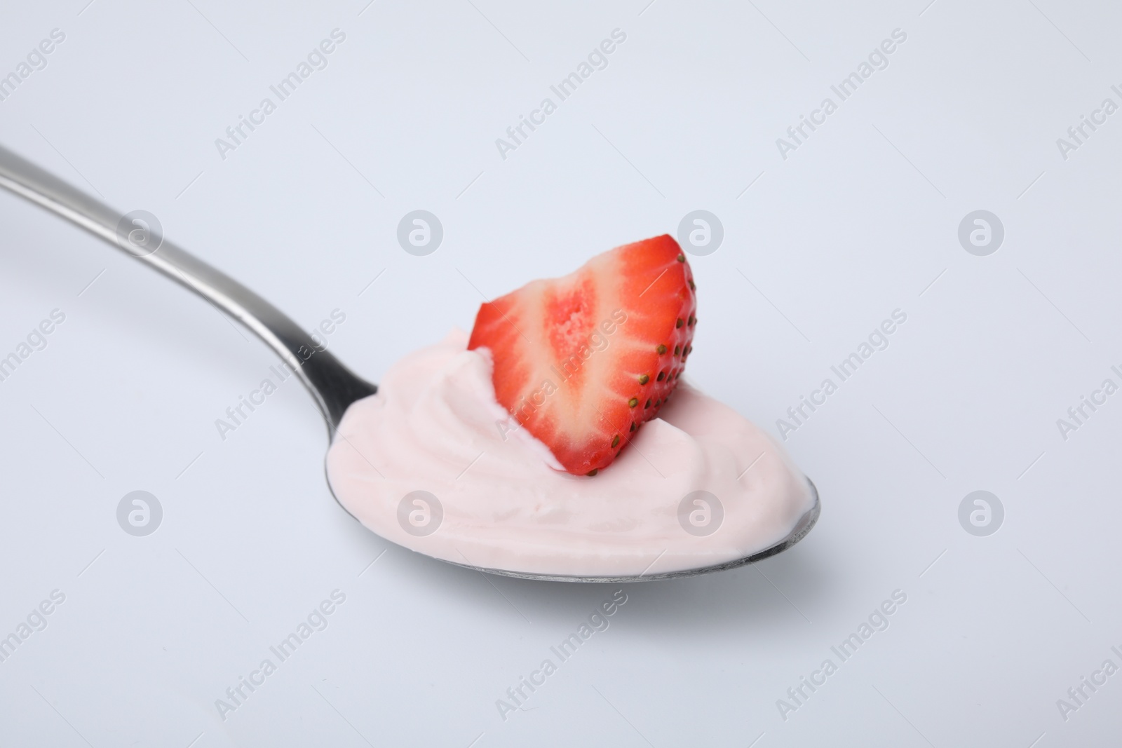 Photo of Delicious natural yogurt with fresh strawberry in spoon on light background