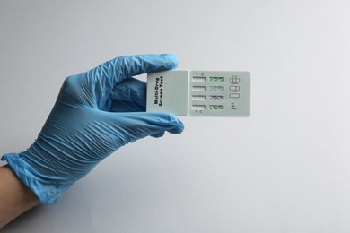 Photo of Doctor holding multi-drug screen test on light grey background, closeup
