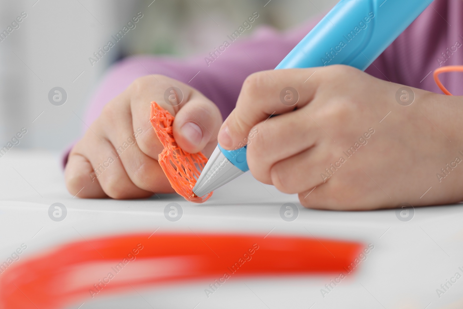 Photo of Girl drawing with stylish 3D pen at white table indoors, closeup