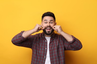 Photo of Happy young man touching mustache on yellow background