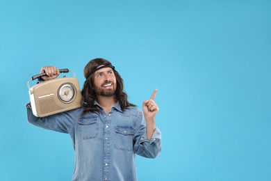 Stylish hippie man with retro radio receiver pointing at something on light blue background, space for text