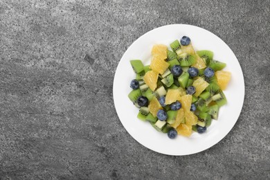 Plate of tasty fruit salad on grey textured table, top view. Space for text