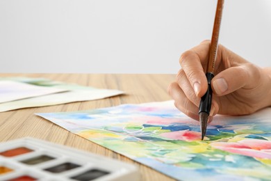 Photo of Woman painting flowers with watercolor at wooden table, closeup. Creative artwork