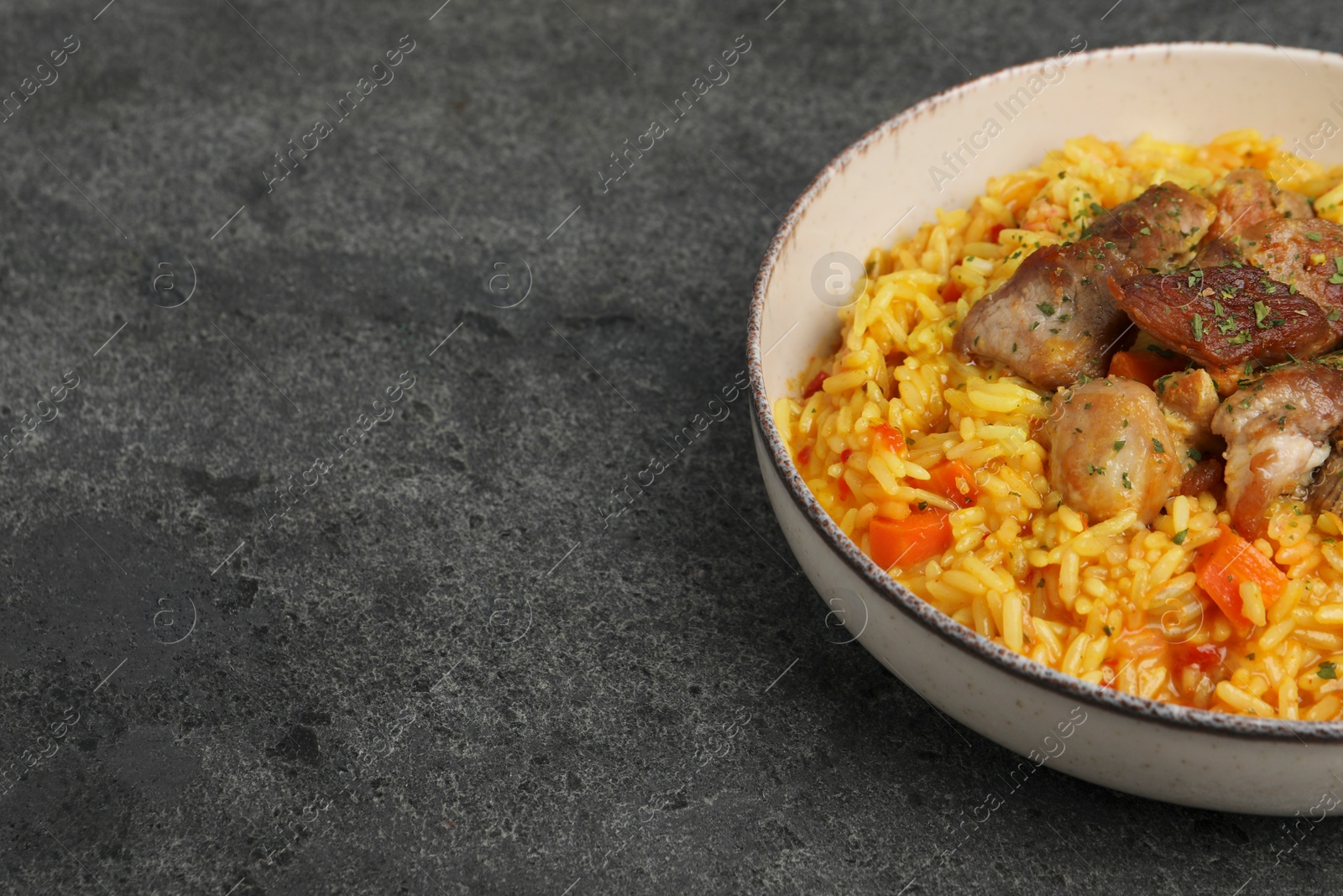 Photo of Delicious pilaf with meat on grey textured table, space for text