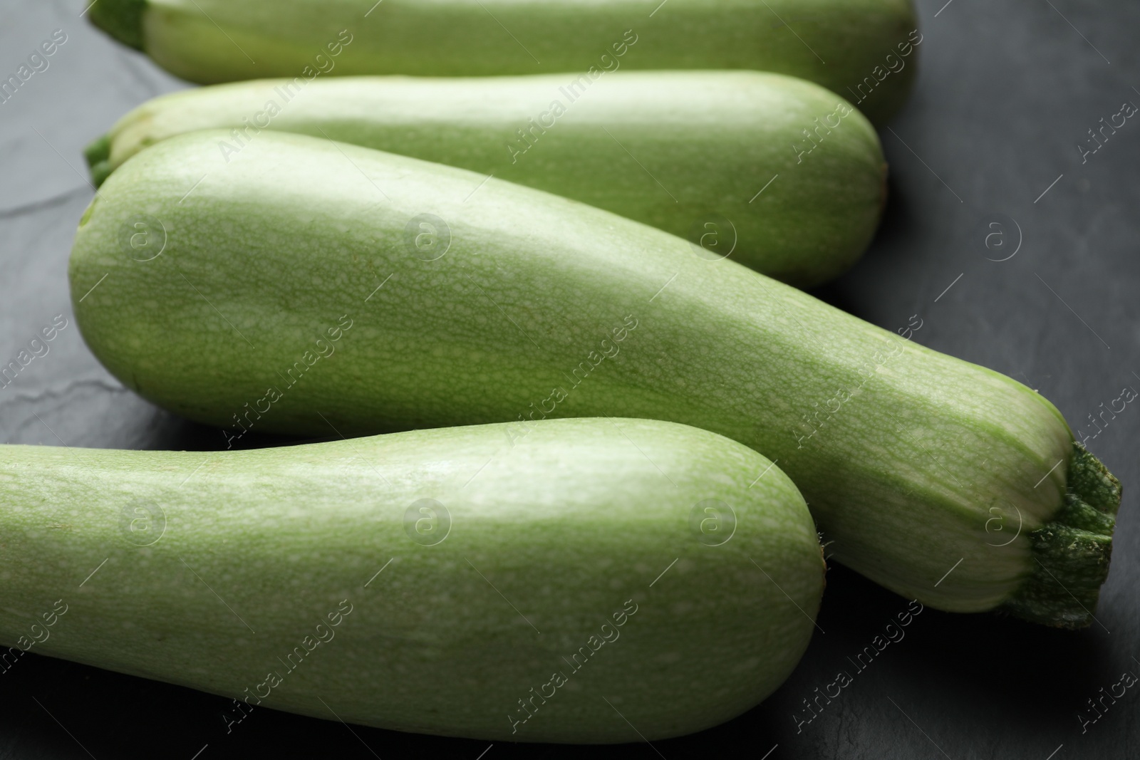 Photo of Raw green zucchinis on black slate table, closeup