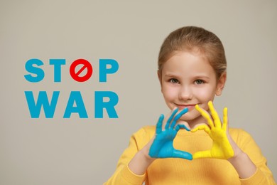 Stop war. Little girl making heart with her hands painted in colors of Ukrainian flag on light background