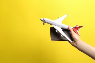 Photo of Woman holding toy airplane and passport on yellow background, closeup. Space for text