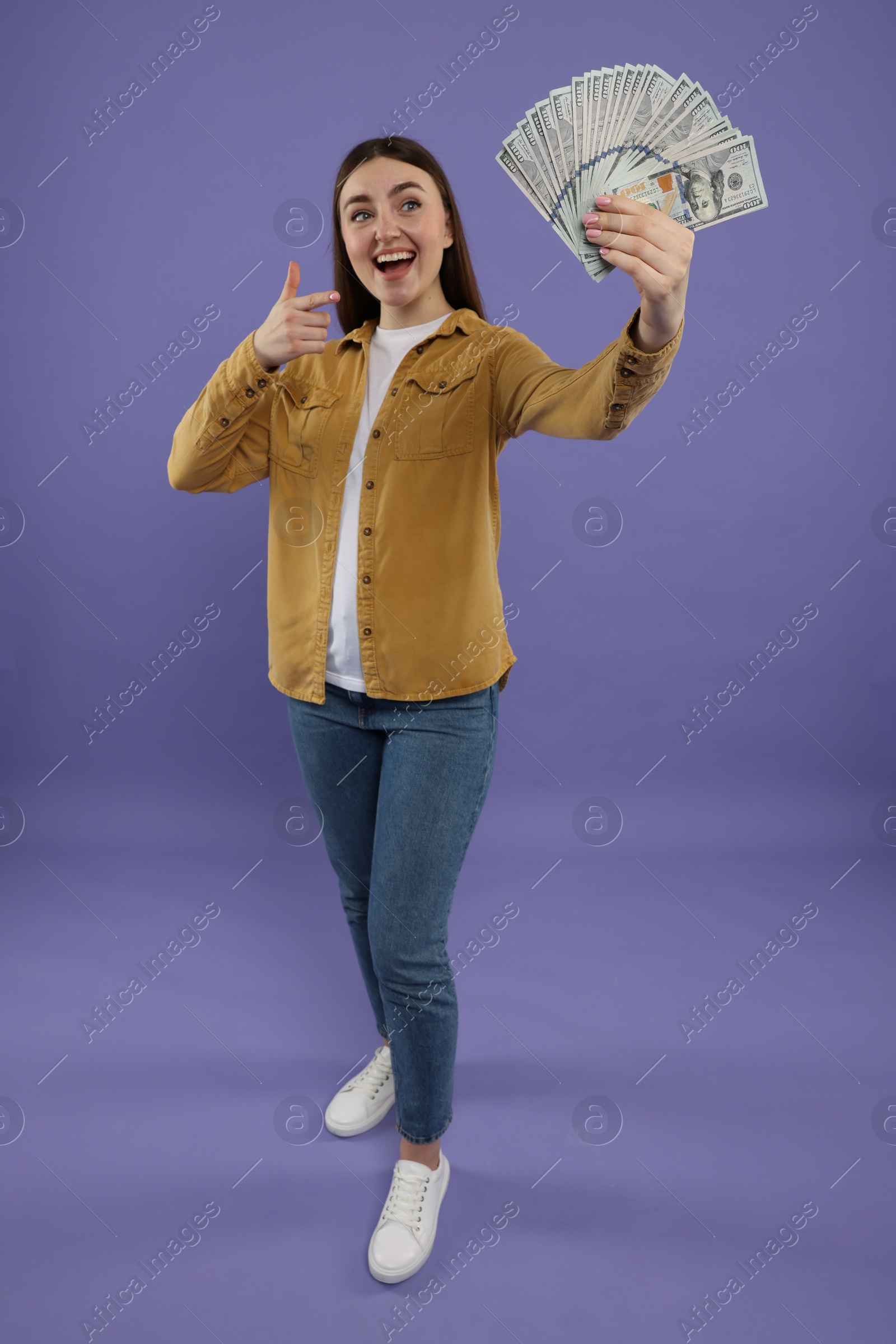 Photo of Happy woman pointing at dollar banknotes on purple background