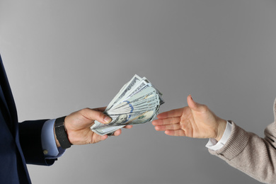 Photo of Man giving bribe money to woman on grey background, closeup