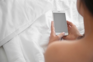 Photo of Young woman holding mobile phone with blank screen in hands on bed