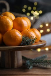 Photo of Stand with delicious ripe tangerines and fir twigs on wooden table