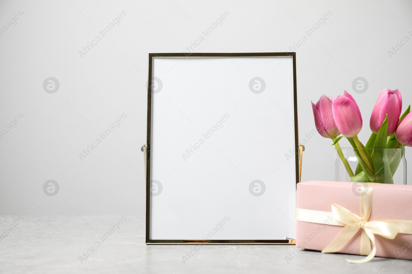 Image of Beautiful tulips, gift and blank photo frame on light table