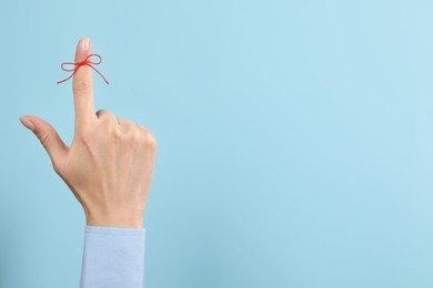 Photo of Woman showing index finger with tied red bow as reminder on light blue background, closeup. Space for text