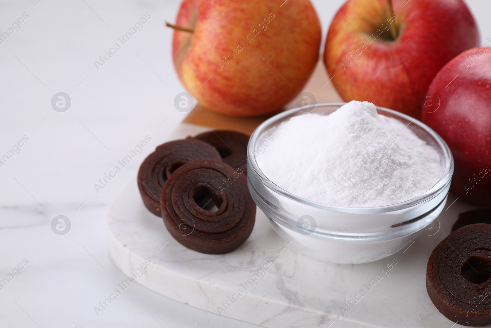Photo of Sweet fructose powder, fruit leather rolls and apples on white marble table, closeup. Space for text