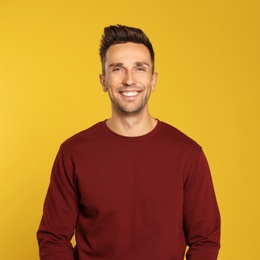 Photo of Happy young man in sweatshirt on yellow background. Winter season