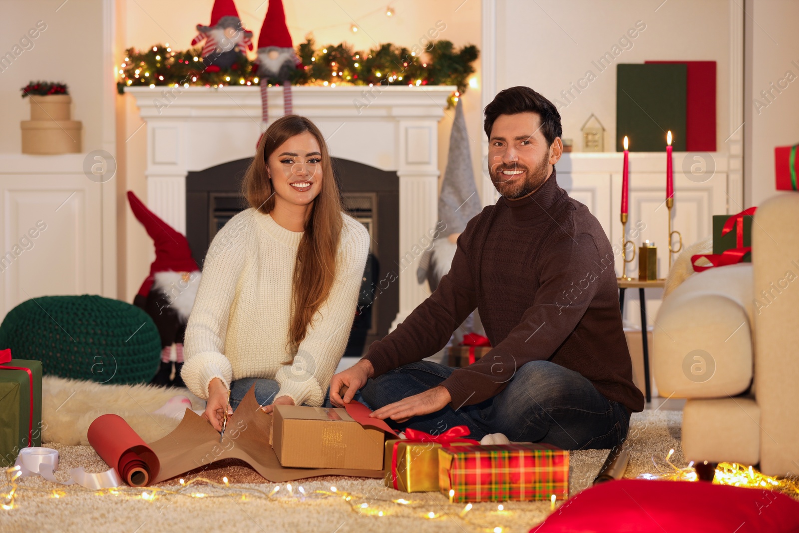 Photo of Happy couple decorating Christmas gift with wrapping paper at home