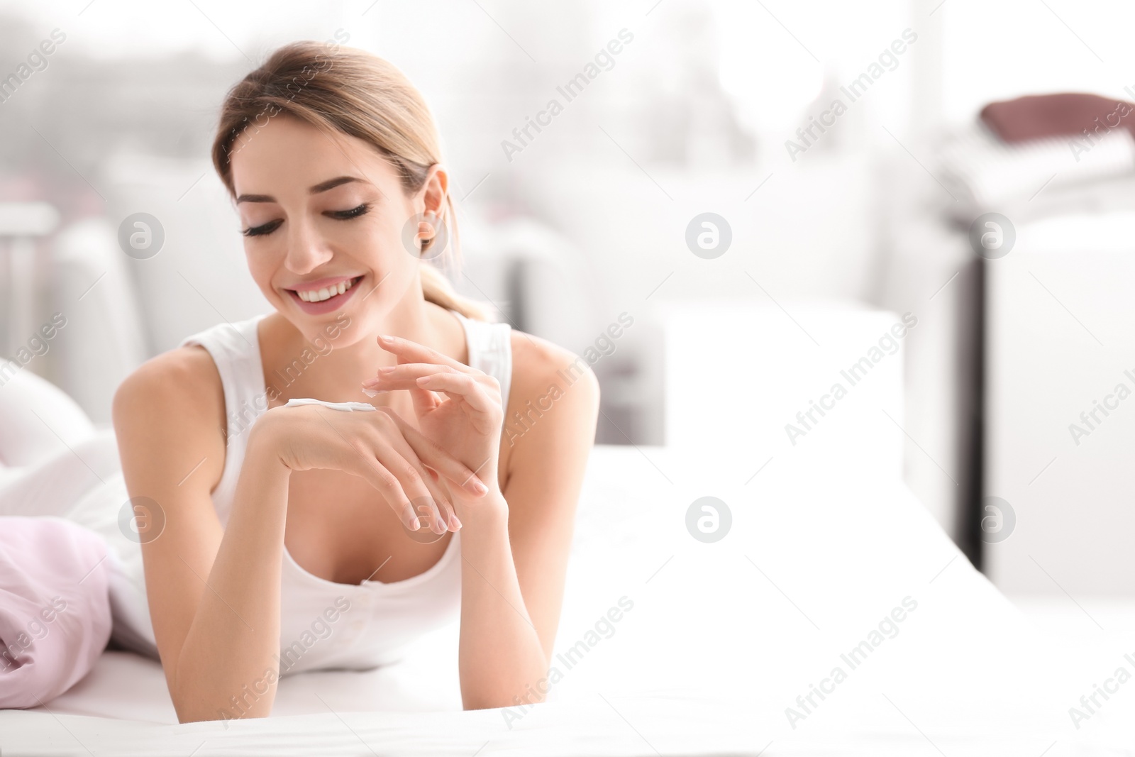 Photo of Young woman applying hand cream on bed at home