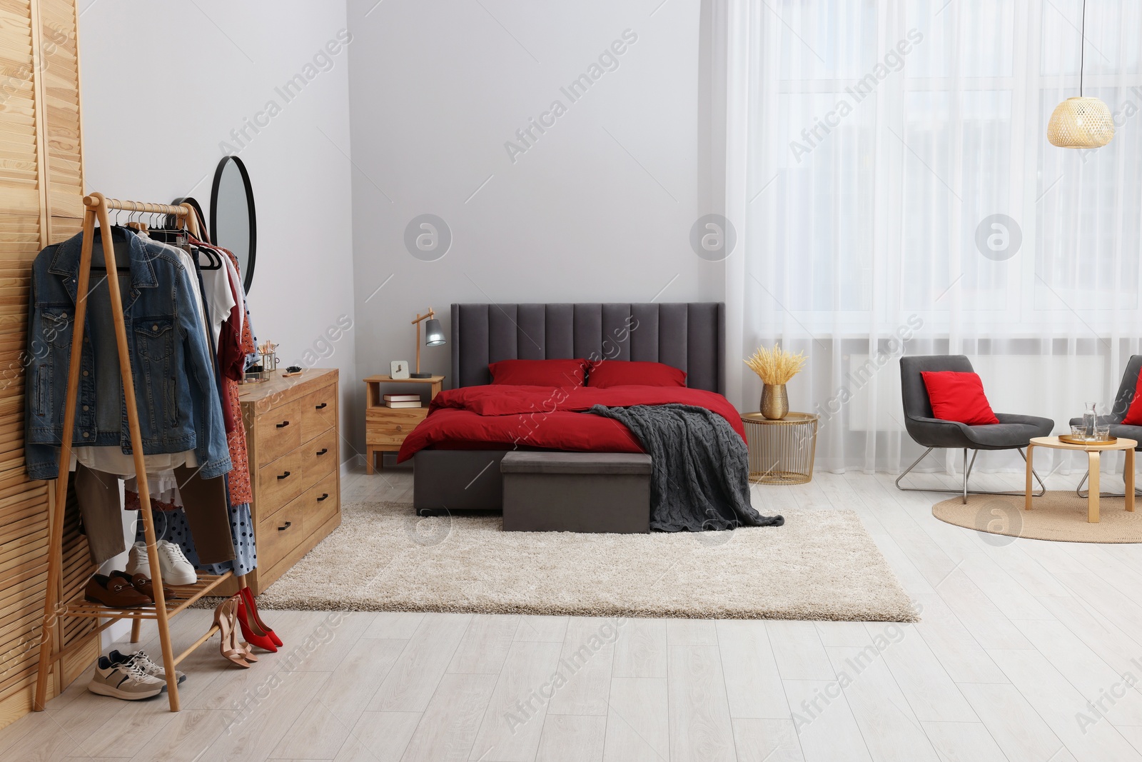 Photo of Stylish bedroom with comfortable bed, wooden chest of drawers and clothing rack. Interior design