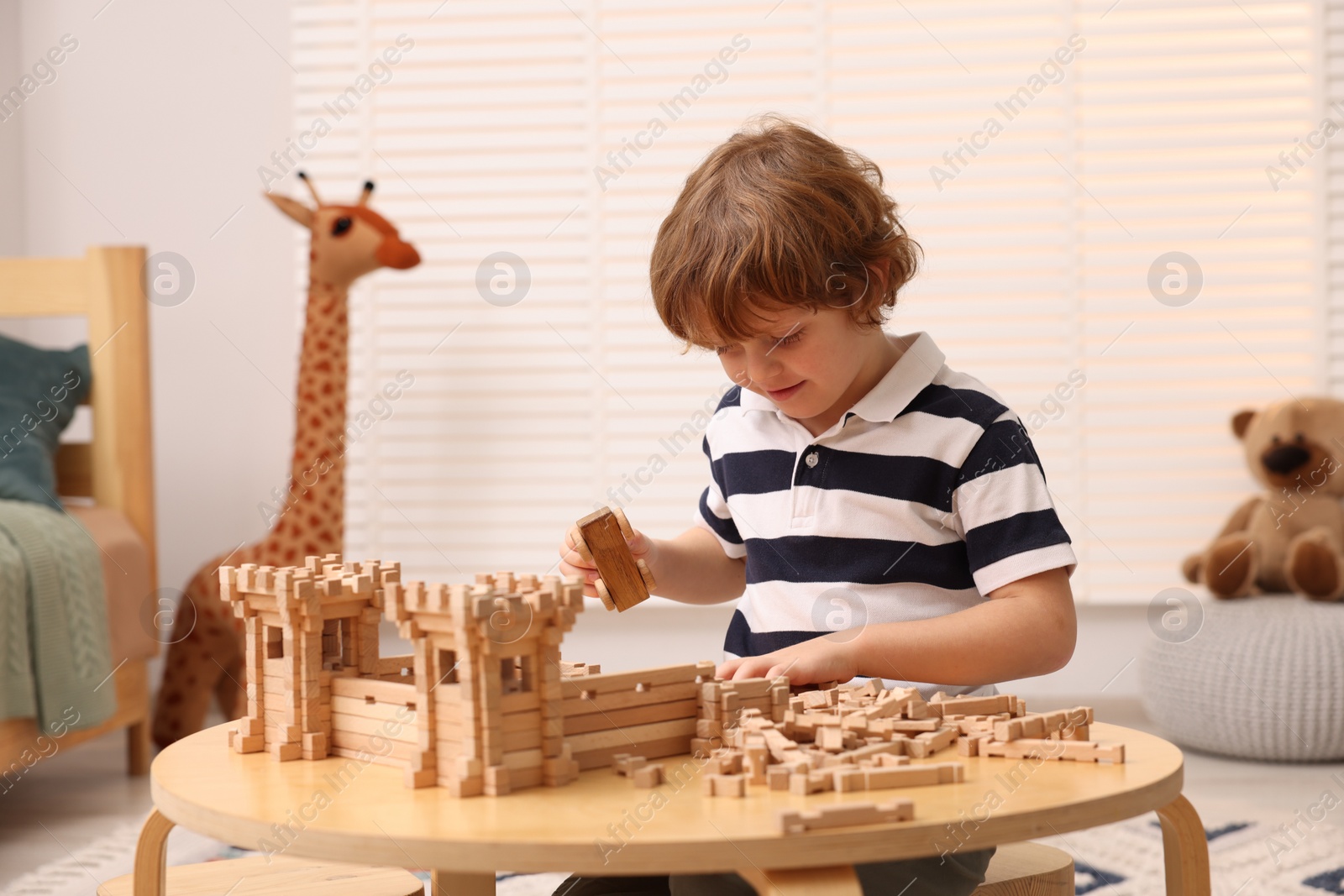 Photo of Cute little boy playing with wooden construction set at table in room. Child's toy