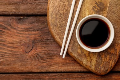 Photo of Bowl with soy sauce and chopsticks on wooden table, top view. Space for text