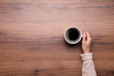 Photo of Woman with cup of coffee at wooden table, top view. Space for text