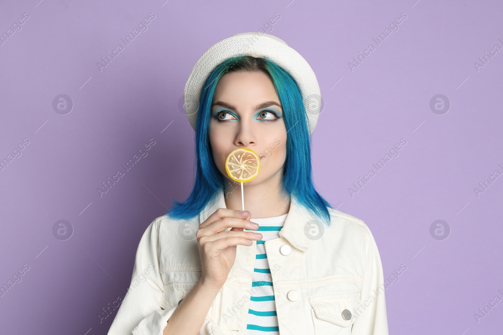 Photo of Young woman with bright dyed hair holding candy on lilac background