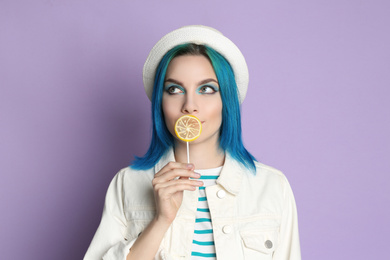 Young woman with bright dyed hair holding candy on lilac background