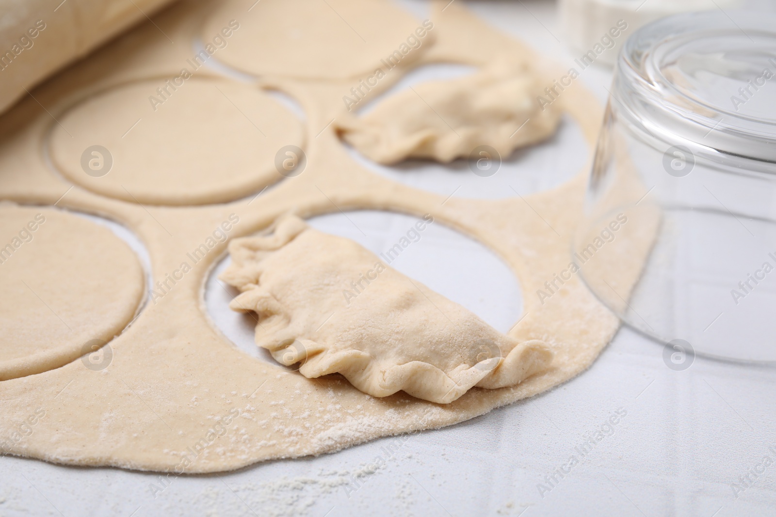 Photo of Process of making dumplings (varenyky) with tasty filling. Raw dough and other ingredients on white tiled table, closeup