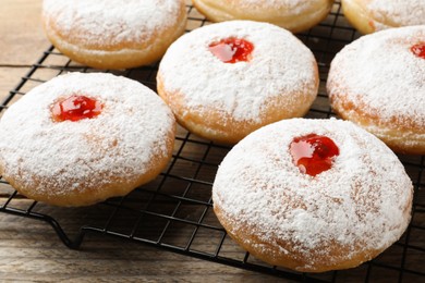 Photo of Many delicious donuts with jelly and powdered sugar on cooling rack, closeup