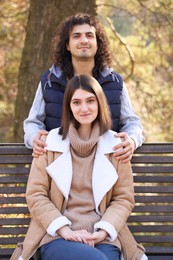 Photo of Young couple spending time together near wooden bench in autumn park. Dating agency