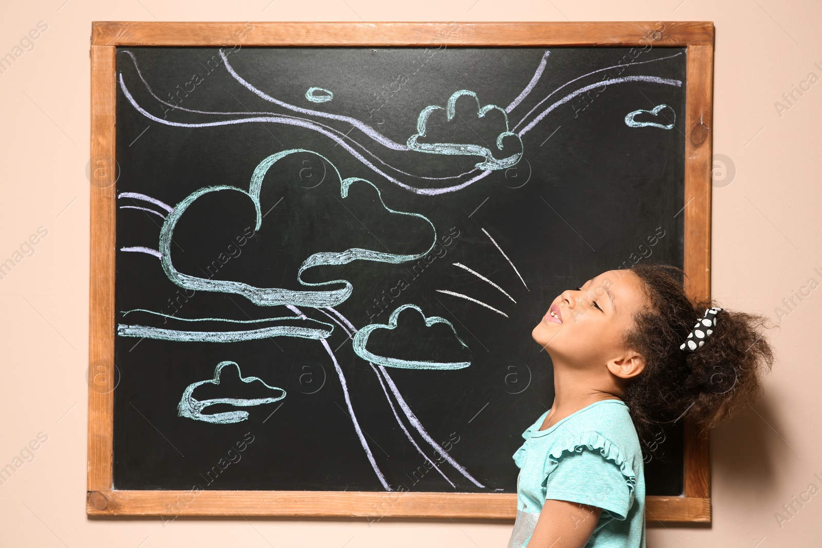 Photo of African-American child playing at blackboard with chalk drawn sky and clouds