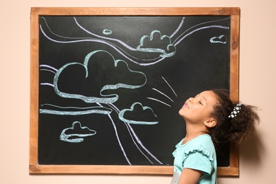 Photo of African-American child playing at blackboard with chalk drawn sky and clouds