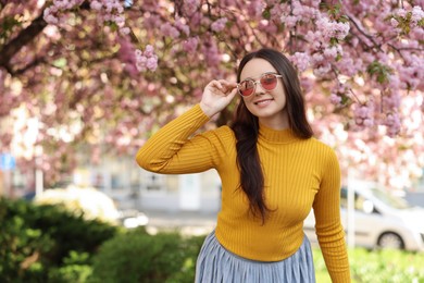 Beautiful woman in sunglasses near blossoming tree on spring day, space for text