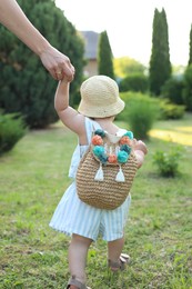 Photo of Cute little girl in stylish clothes holding mother's hand outdoors on sunny day, back view