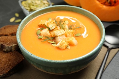 Delicious pumpkin soup in bowl served on black table, closeup