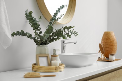 Vase with eucalyptus branches and toiletries near vessel sink in bathroom. Interior design