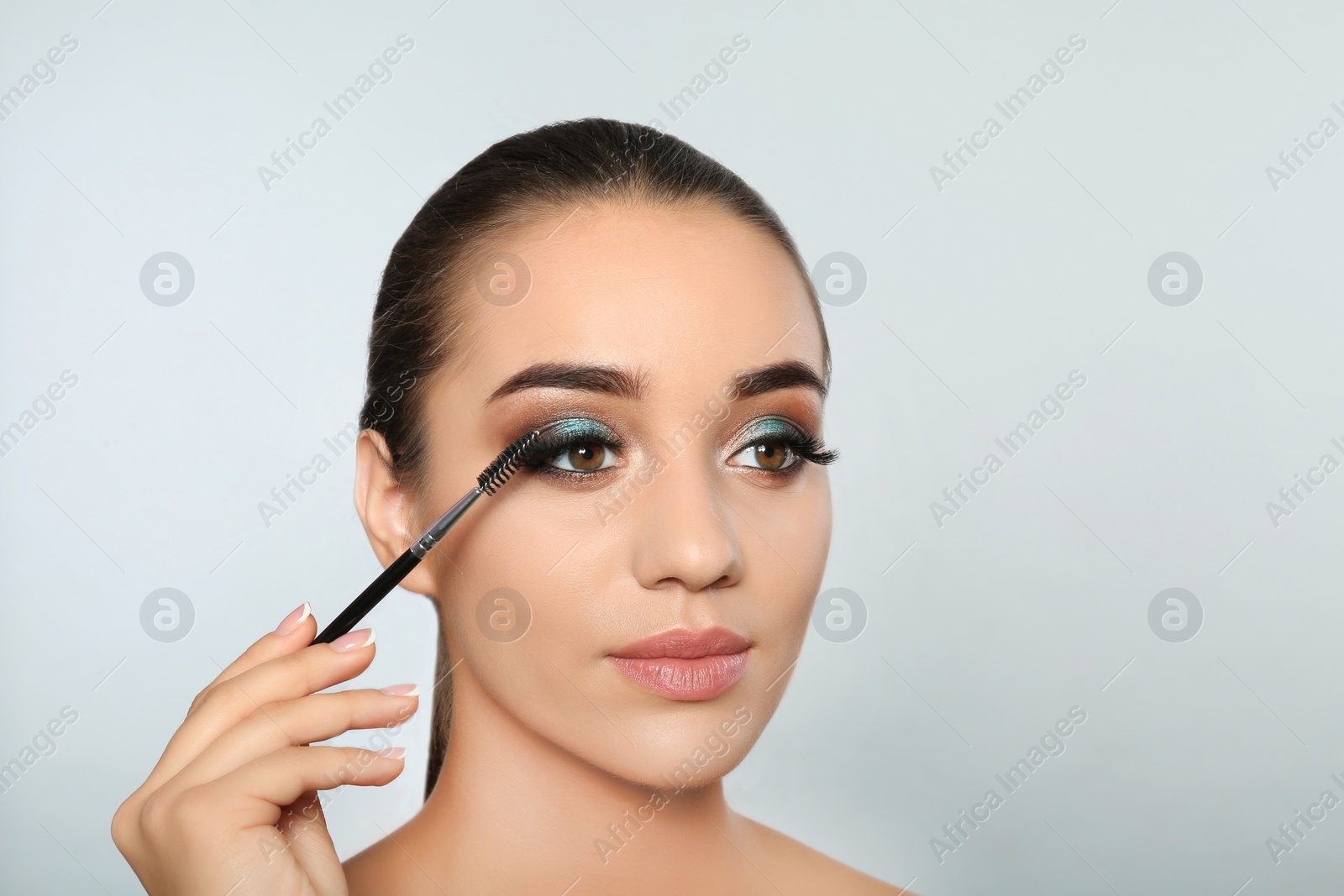 Photo of Portrait of young woman brushing eyelash extensions on light background. space for text