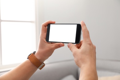 Man holding smartphone with blank screen indoors, closeup of hands. Space for text