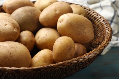 Photo of Raw fresh potatoes in wicker basket on light blue wooden table, closeup