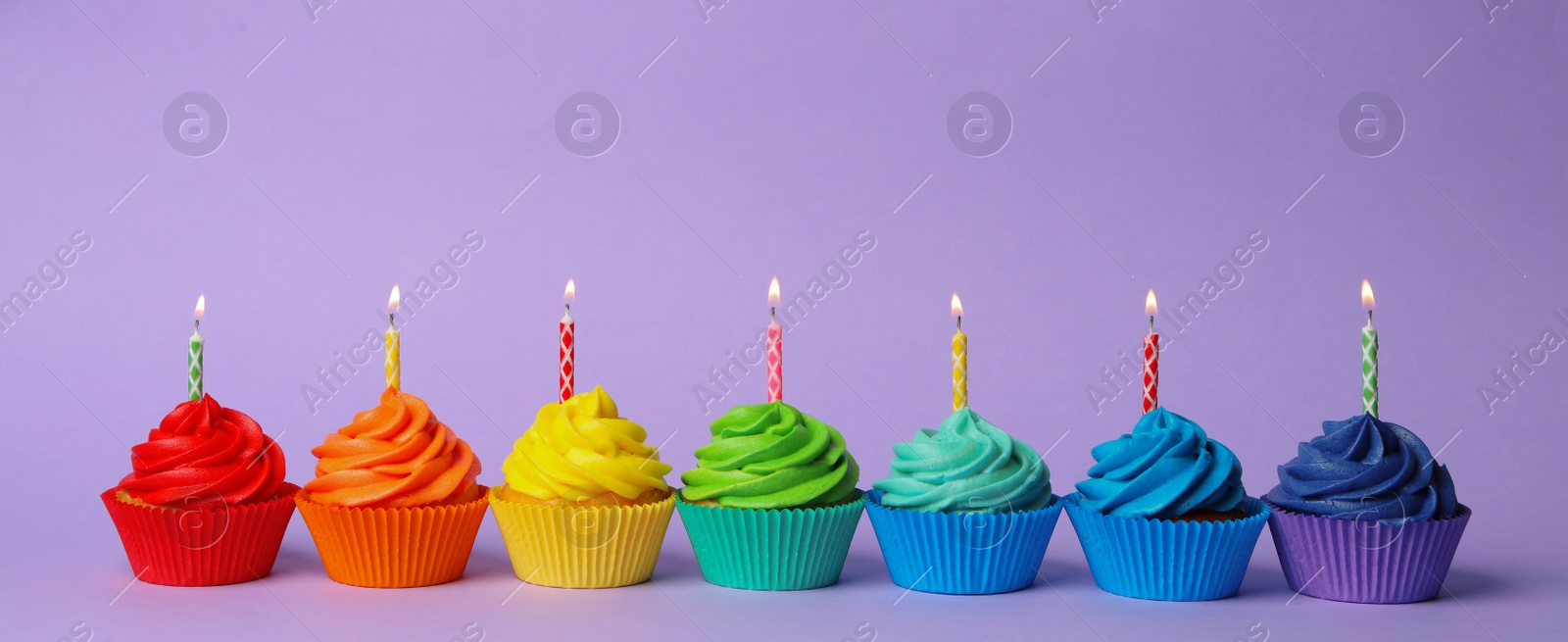 Photo of Delicious birthday cupcakes with burning candles on violet background