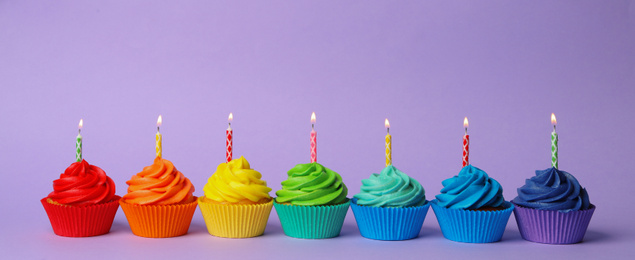 Photo of Delicious birthday cupcakes with burning candles on violet background