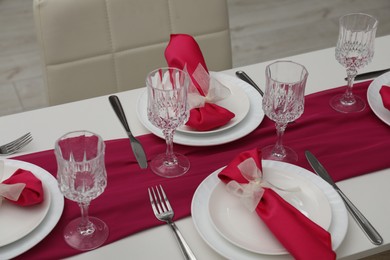 Photo of Color accent table setting. Glasses, plates, cutlery and pink napkins in dining room