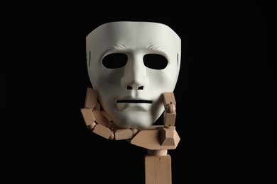 Photo of Wooden mannequin hand holding plastic mask on black background. Theatrical performance