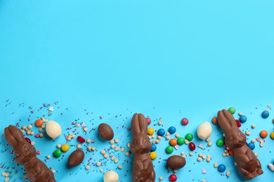 Photo of Flat lay composition with chocolate Easter bunnies, eggs and candies on light blue background. Space for text
